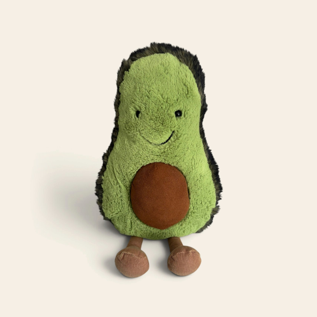 Amuseables Avocado A2A: a plush avocado half toy with dark green fuzzy skin, a pale green middle, a brown stone, a smiling face and brown corduroy legs