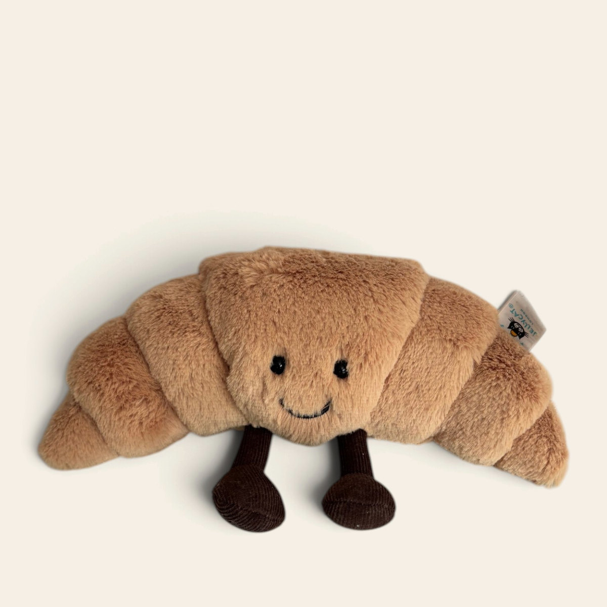 Amuseables Croissant A6C: a golden brown plush croissant toy with a smiling face and dark brown legs