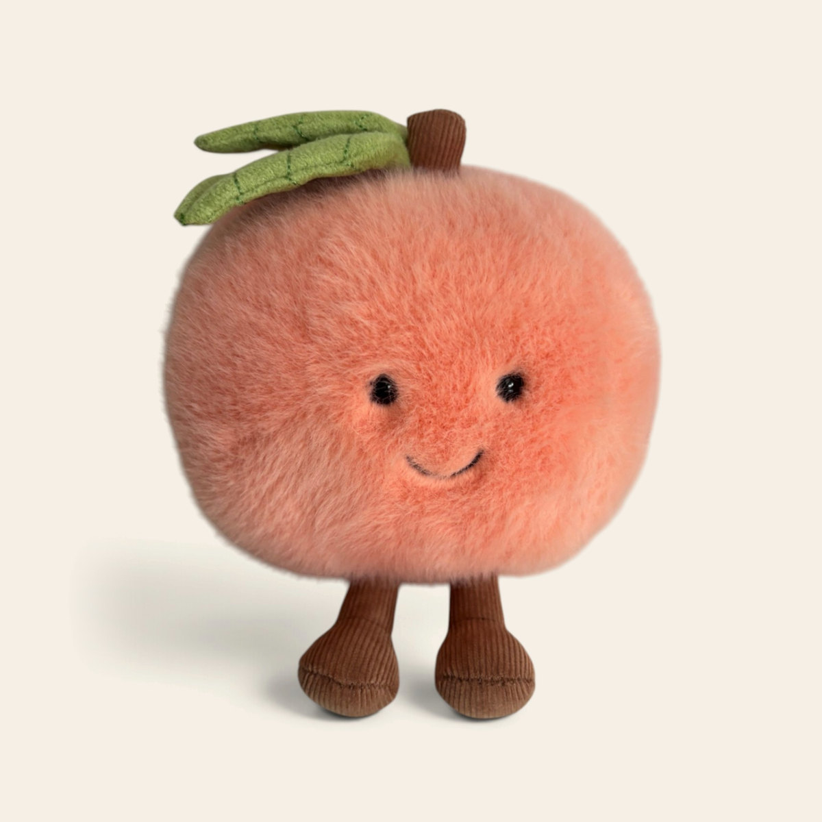 Amuseables Peach A6PEACH: a round orange-pink fluffy plush peach toy with a green leaf, a smiling face and brown corduroy legs