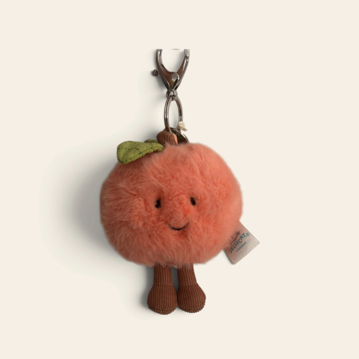 Amuseables Peach Bag Charm APEACH4BC: a small orange-pink fluffy plush peach with a green leaf, a smiling face, brown corduroy legs and a metal clip
