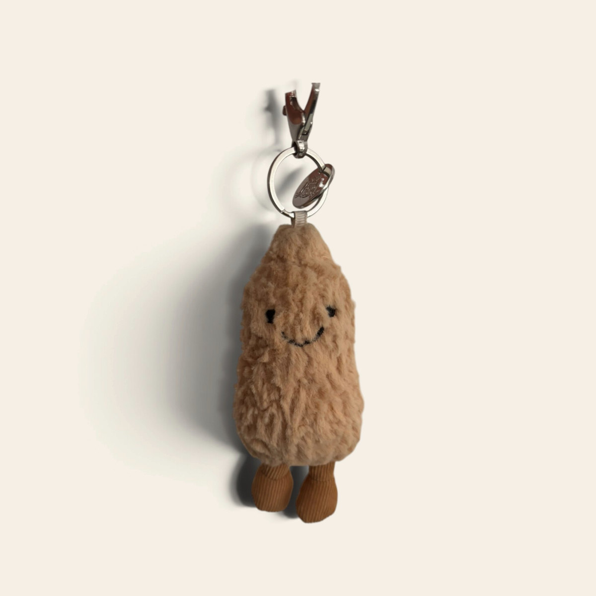Amuseables Peanut Bag Charm APN4BCH: a small beige fuzzy plush peanut with a smiling face, brown corduroy legs and a metal clip