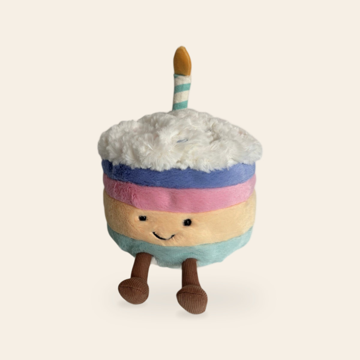 Amuseables Rainbow Birthday Cake A2RBC: a plush cake toy with blue, pink, peach and mint layers, fluffy white icing, a striped candle, a smiling face and brown corduroy legs