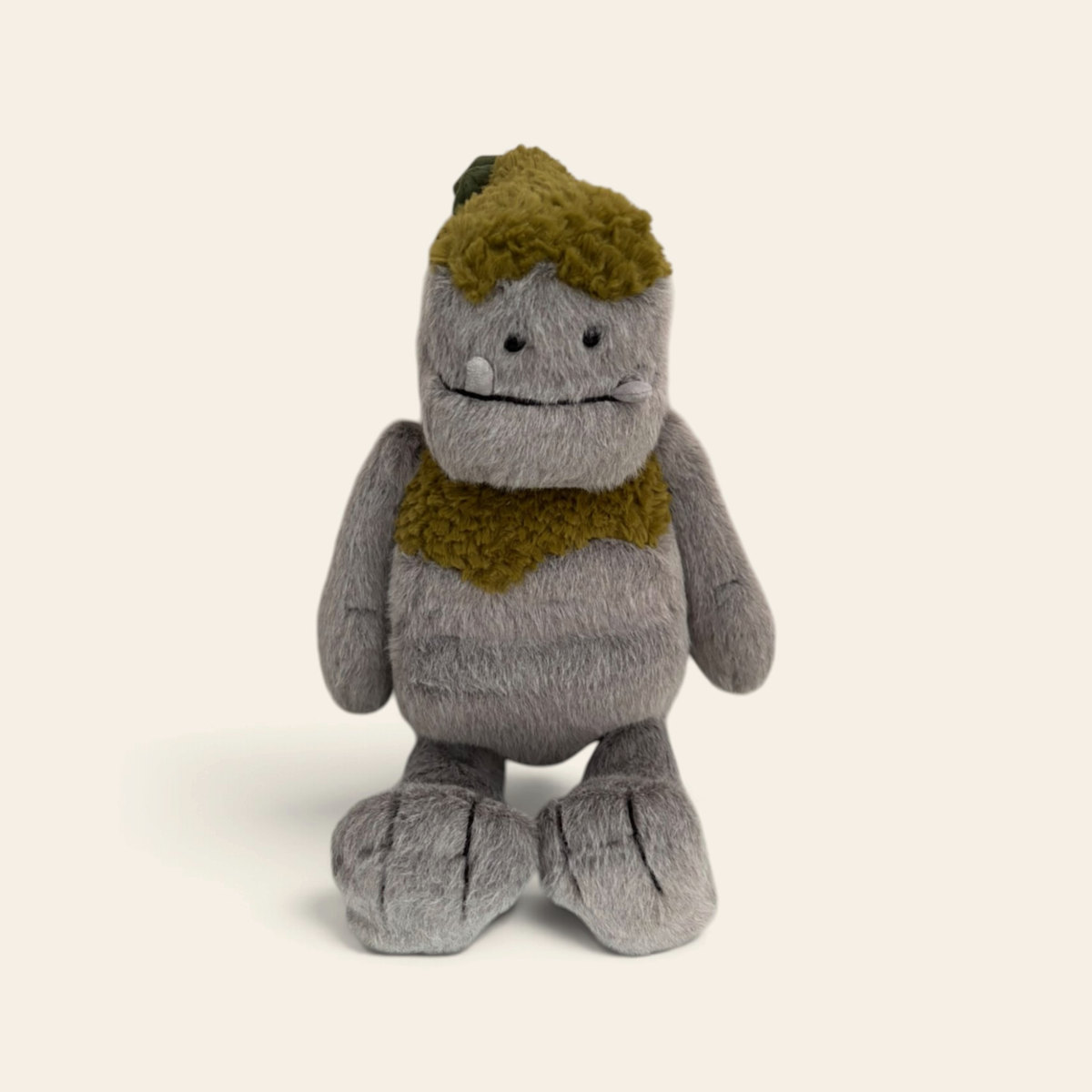 Rockleton R3RMON: a grey plush rock monster with a mossy green top and collar and a gentle smiling face, standing